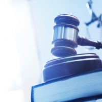 A gavel rests on top of a stack of law books with a statue of lady justice out of focus in the background.