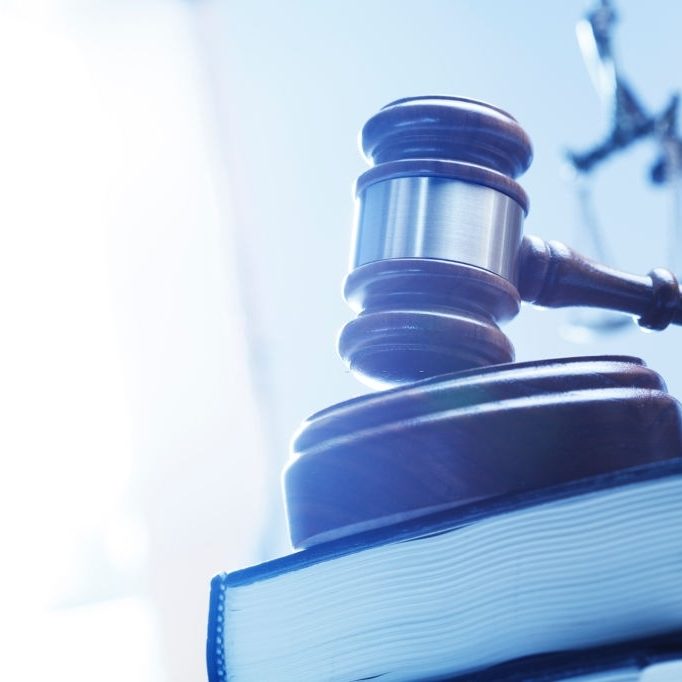 A gavel rests on top of a stack of law books with a statue of lady justice out of focus in the background.
