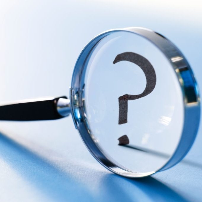 A question mark seen through a magnifying glass. Photographed with a very shallow depth of field.